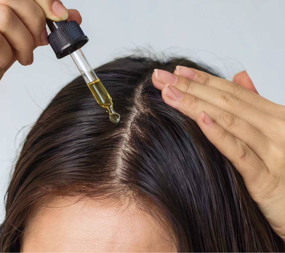 A dropper of KAYN argan oil applied along the parting of dark hair.
