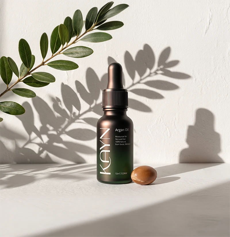 The 10ml Kayn Argan Oil bottle beside an argan nut, against a sunlit plaster wall.