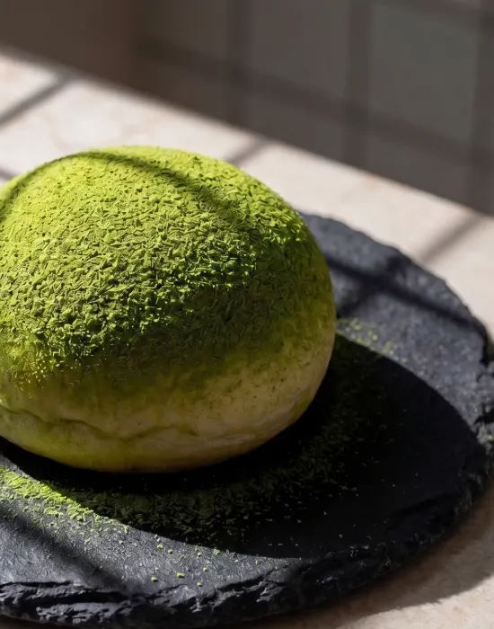 An Uji matcha mochi bun dusted with ceremonial matcha on a slate plate